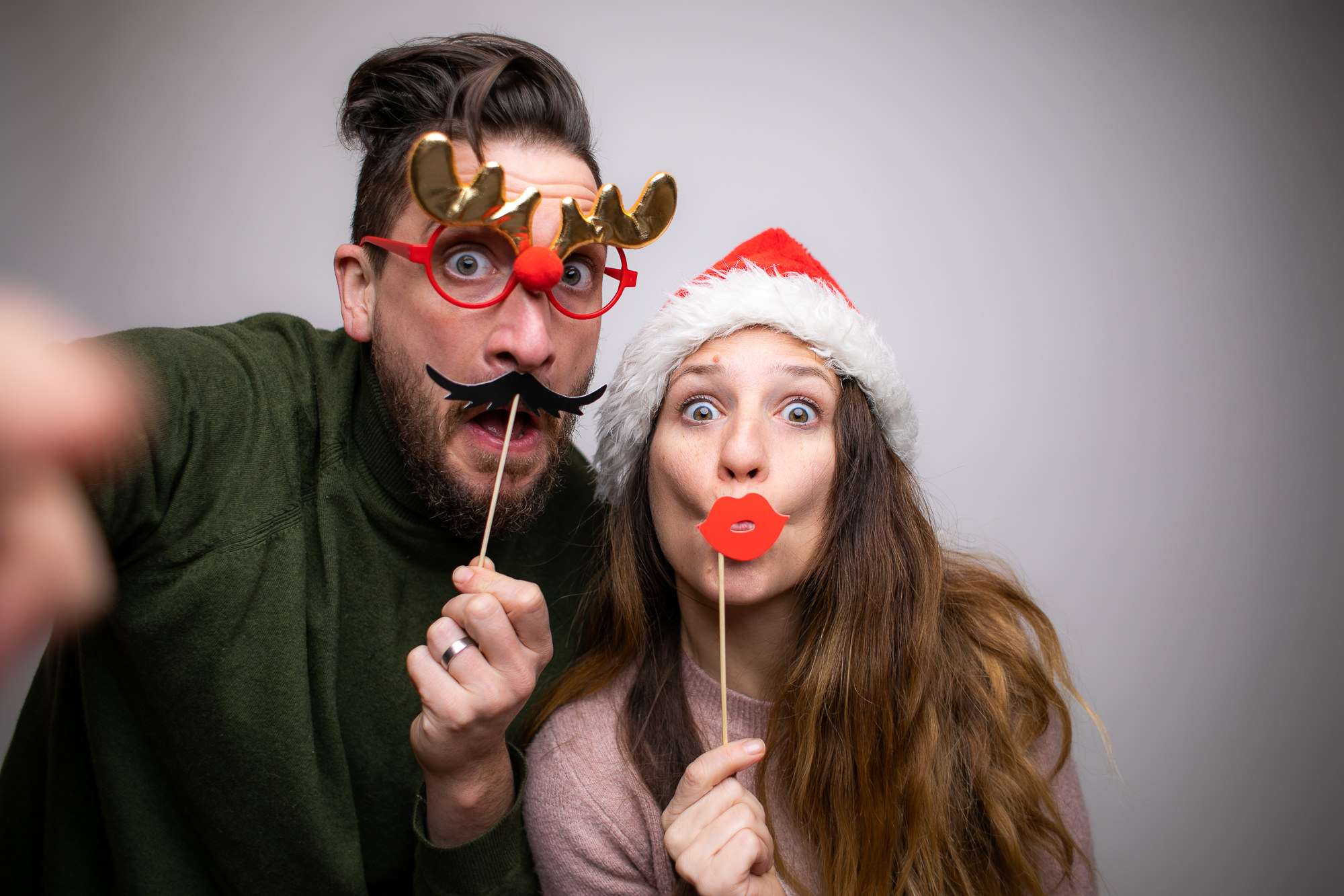 Zwei Personen mit großen Sonnenbrillen und falschen Schnurrbärten posieren lachend vor der Fotobox.