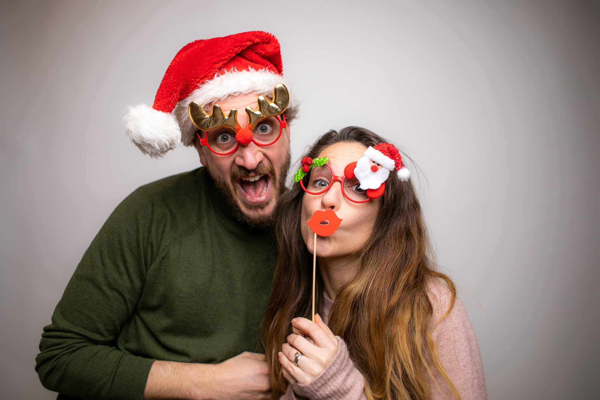 Zwei Personen mit bunten Perücken und Herzbrillen lachen gemeinsam vor der Fotobox.