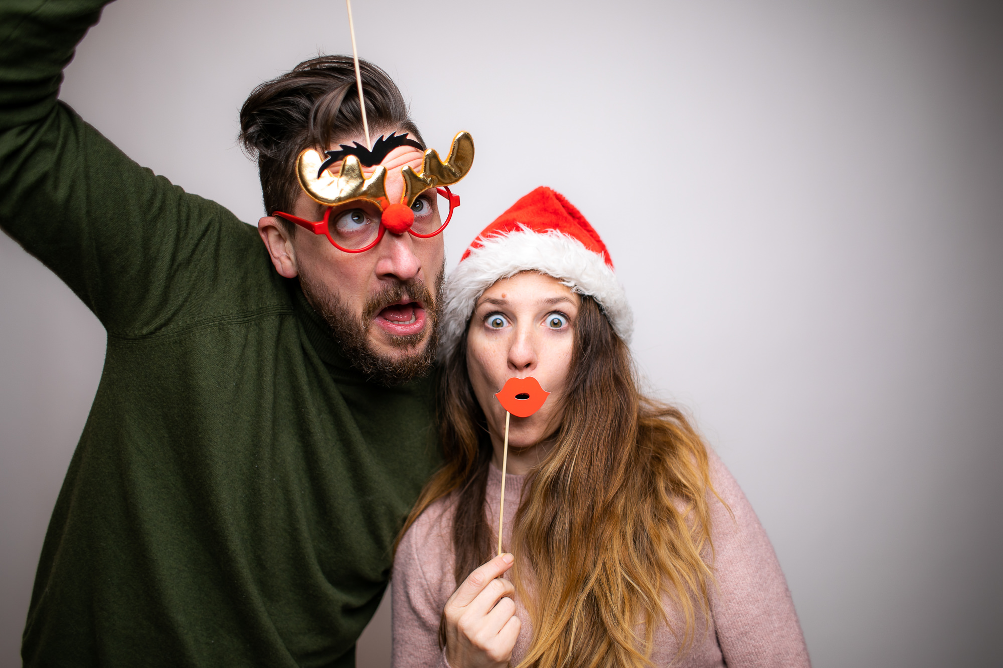 Zwei Personen mit Weihnachtsmützen und Rentiergeweih-Requisiten vor der Fotobox.