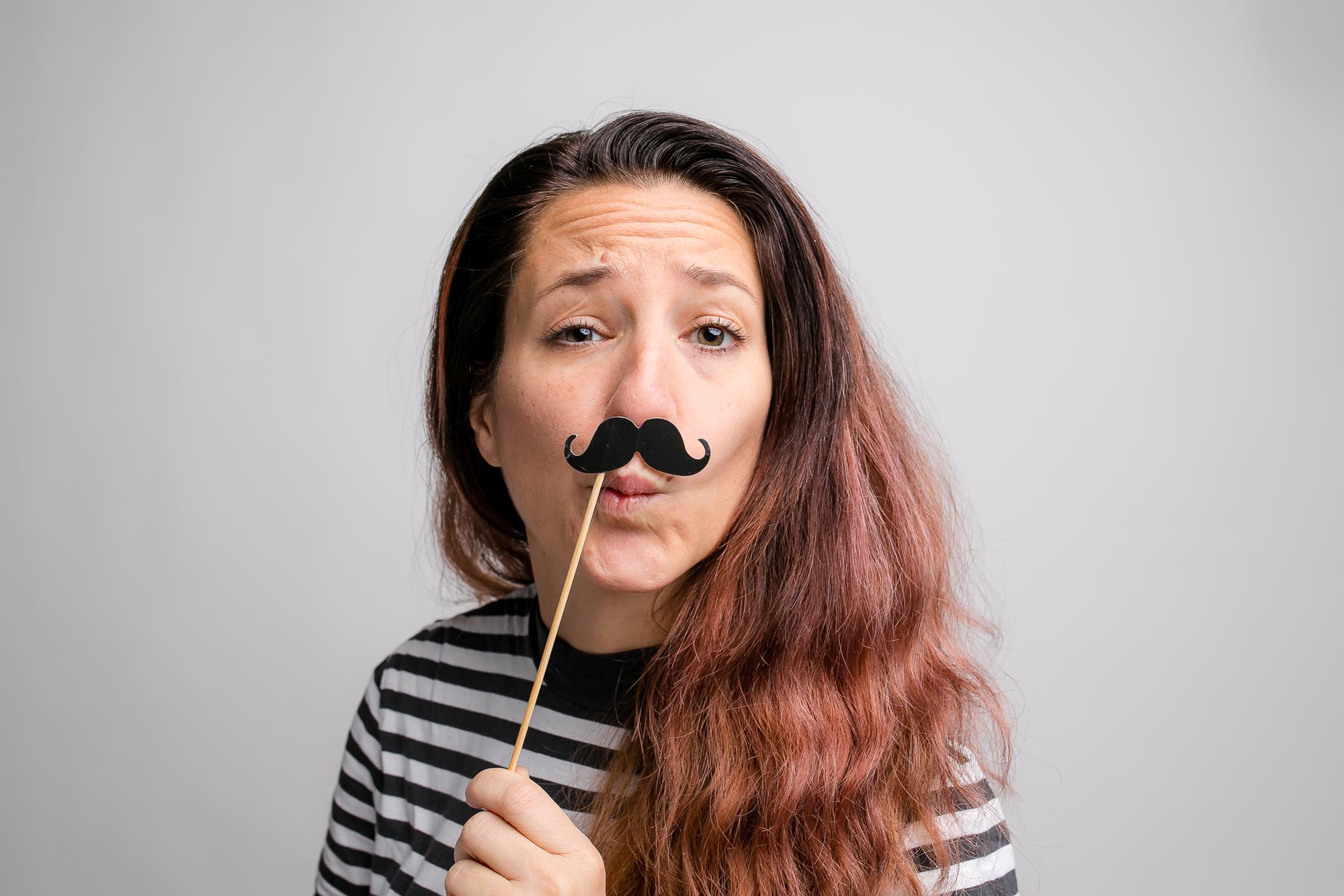 Zwei Freunde mit falschen Schnurrbärten und Zylinderhüten stehen vor der Fotobox.